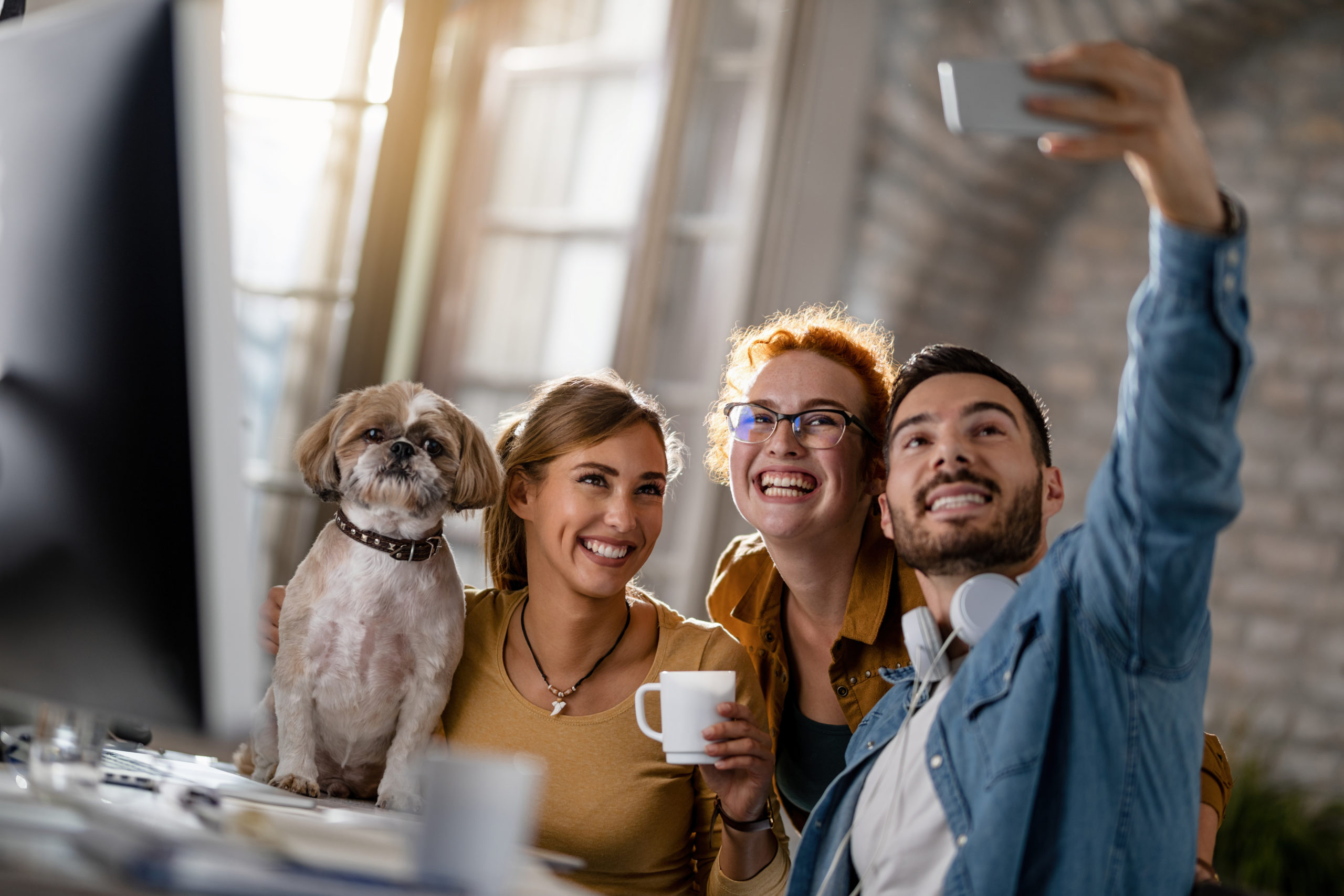 Group of happy freelancers with a dog taking selfie in the offic